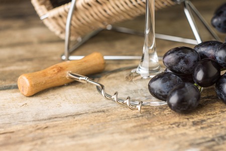 Corkscrew with grapes and wineglass on wooden table