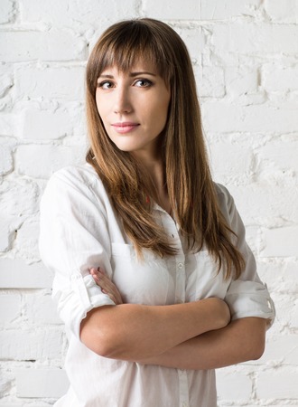 Young pretty woman standing against white brick wall. Beauty caucasian hipster girl posing in studioの写真素材