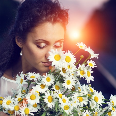 Toned image of young beautiful dreamy women with bouquet of flowers. Pretty caucasian girl with bunch of chamomile at sunsetの写真素材