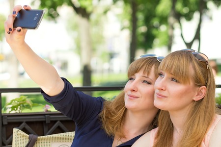 Two twins girls taking selfie in restaurant at sunny summer day. Young pretty sisters on terrace of...