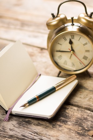 Open small notebook with retro-fashioned fountain pen and alarm clock behind. Writing vintage backgroundの写真素材
