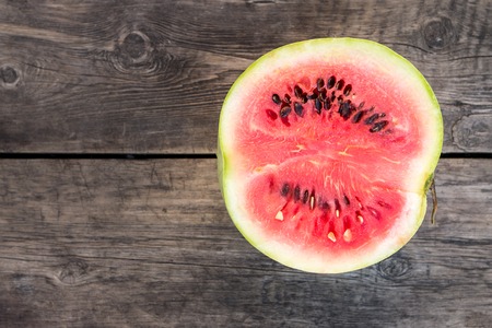 Cut in half watermelon on old wooden table. Red ripe fruit on wood background with copy space top view imageの写真素材