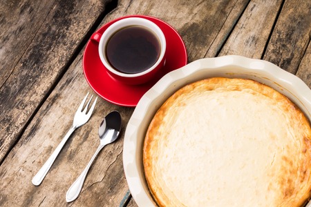 Baked cheesecake in ceramic cake pan with cup of tea on wooden tableの写真素材