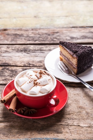 Hot cocoa with marshmallows and slice of chocolate cake on wooden background. Close up image of hot beverage with dessert in cafe or restaurantの写真素材