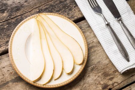 Sliced ripe pear on saucer with silverware on wooden table. Top view dessert fruit image gourmet menu backgroundの写真素材