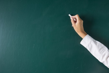 Female hand writing with a piece of chalk on the blackboard or chalkboard. School background with copy spaceの写真素材