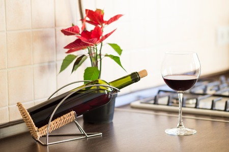 Glass of red wine with bottle and plant in pot on the kitchen worktop near stoveの写真素材
