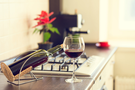 Glass of red wine with bottle and plant in pot on the kitchen worktop near stoveの写真素材