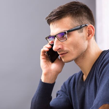 Young business man in glasses speaking on the phone. Adult caucasian man talking on cellphone at his...