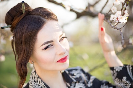 Beautiful young woman with japanese style make-up. Asian girl with blooming tree on spring dayの写真素材