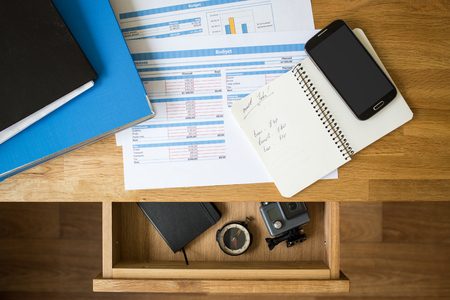 Office accounting stuff vacation concept background. Accounts, smartphone  and binders on the desktop and compass with action camera in the open drawerの写真素材