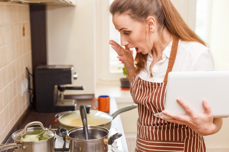 Young woman trying cooking with recipe from laptop. Shocked caucasian woman online learning cookingの写真素材