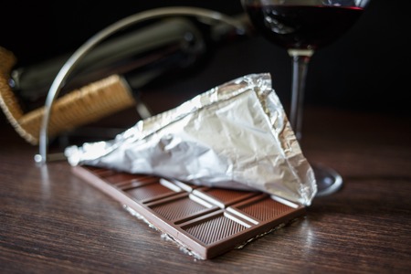 A chocolate bar in foil with glass of red wine on wooden tableの写真素材