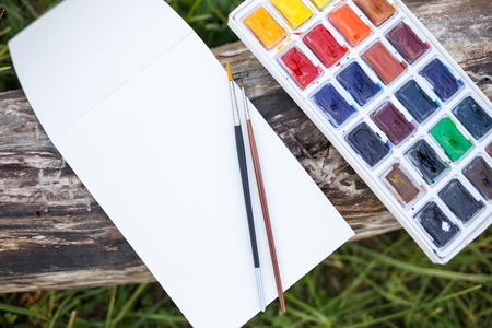 Mock up with blank paper notebook and watercolor set with brushes lying on the old wood. Top view imageの写真素材