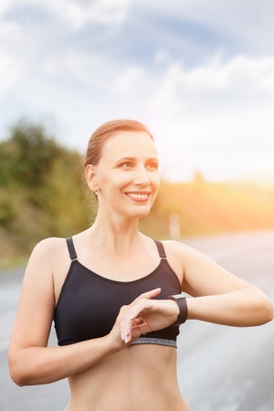 Young smiling fitness woman using her smart watch for heartrate after jogging. Healthy caucasian girl with fitness tracker watchの写真素材