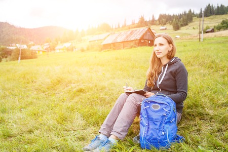 Young hiker woman with backpack writing or sketching into notebook resting on hillの写真素材