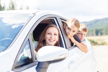 Happy young woman and her children sitting in a car and look out from windows. Family travel background imageの写真素材