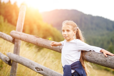 Young teenage girl enjoying holidays in mountains standing near fence in the morningの写真素材