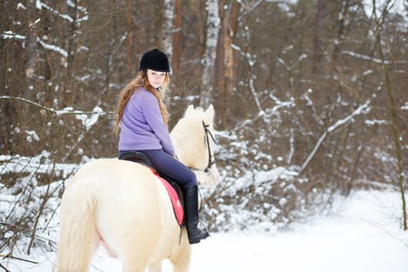 Young rider girl on albino horse in winter forestの写真素材