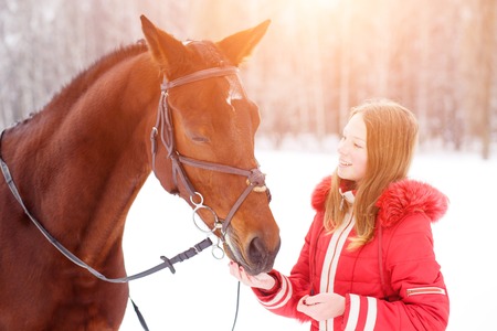 Teenage girl feeding bay horse on winter fieldの写真素材