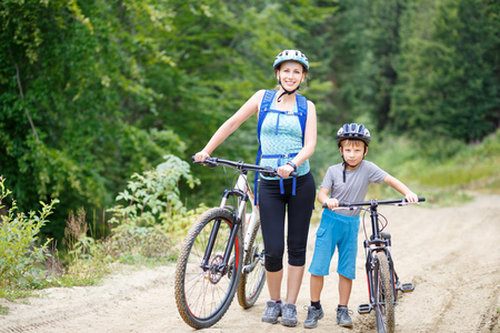 Young woman with son standing with bikes in forestの写真素材