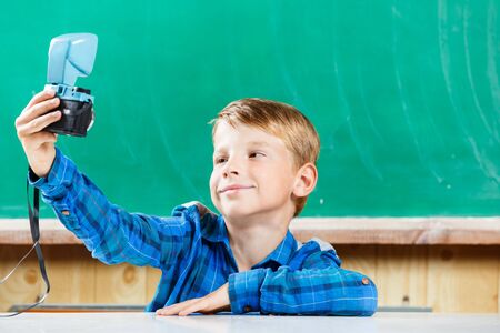 Schoolboy in blue shirt make selfie at blackboard in school. Back to school concept background