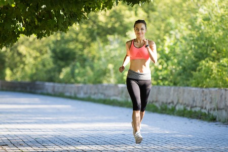 Beautiful young woman in pink top jogging in parkの写真素材