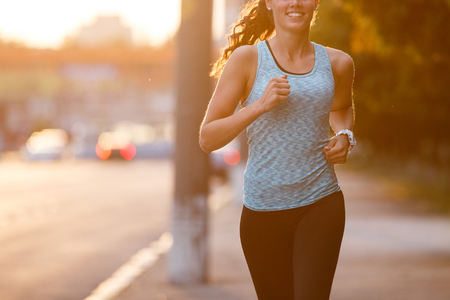 Young smiling sporty woman running on pavement in the morning. Fitness girl jogging in parkの写真素材