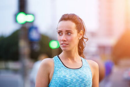 Portrait of young sporty woman resting after jogging in the evening city. Portrait of athletic girl in blue top at sunsetの写真素材