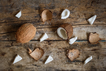 Fresh coconuts with spreaded chops, meat, flakes and shell parts on wooden backgroundの写真素材