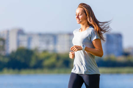 Young smiling sporty woman running in park in the morning. Fitness girl jogging in parkの写真素材