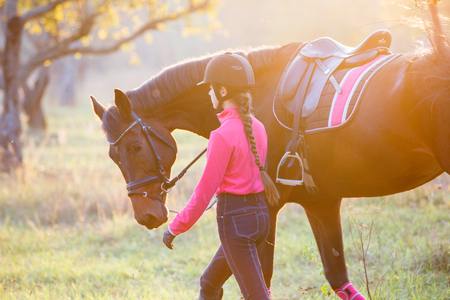 Rider girls walking with horse in sunny parkの写真素材