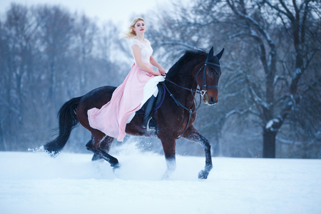 Young woman in dress riding horse on winter fieldの写真素材