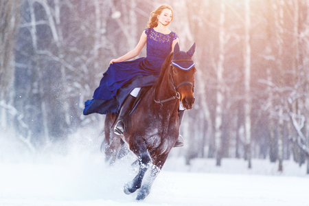 Young girl in dress riding horse on winter fieldの写真素材