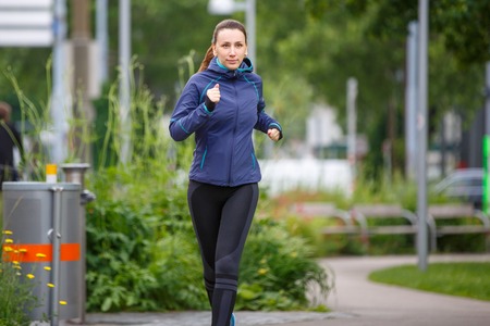 Young woman in blue jacket jogging in park