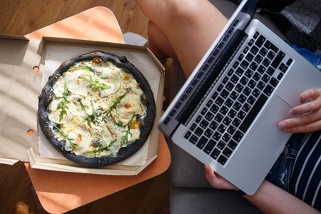 Young woman working on laptop with delivered pizzaの写真素材