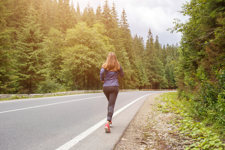 Young slim woman jogging in mountains. Rear viewの写真素材