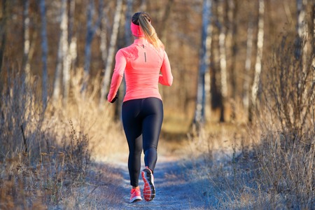 Rear view of young running woman in winter parkの写真素材