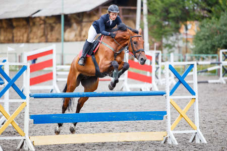 Young woman riding horse jumping over hurdle on show jumping competitionの写真素材