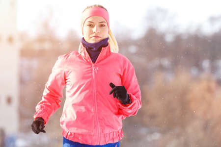 Young girl on trail running training in winter park. Sporty woman running in cold weatherの写真素材