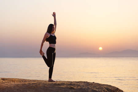 Young woman practicing yoga asana pose in the morning at the sea.の写真素材
