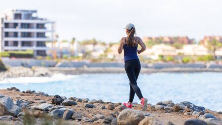 Young sporty woman jogging near the ocean. Back view of running girl with copyspace