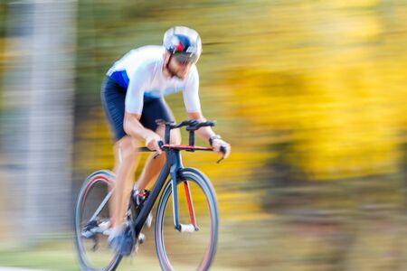 Panning shot of sportsman riding a bike in autumn park. Motion speed cycling blur backgroundの写真素材