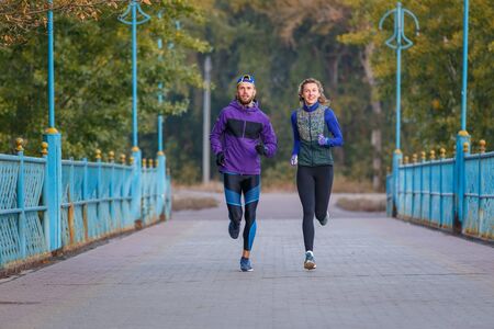 Man and woman running in the autumn park in the morning. Jogging couple outdoors fitness trainingの写真素材