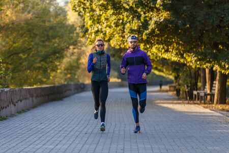 Young fit couple running in autumn park in the morning
