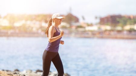Young slim female runner near the sea jogging in the morning. Healthy lifestyle background with copy spaceの写真素材