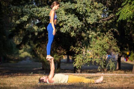 Acroyoga couple balancing on hans in the park. Yoga man and woman practicing acroyoga in summerの写真素材