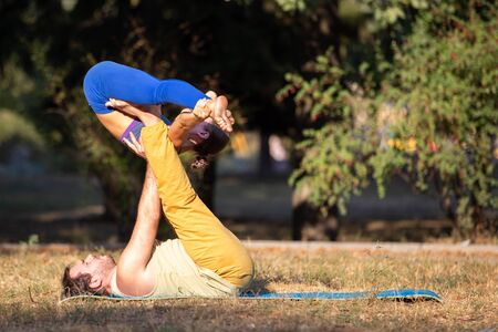 Young fitness couple practicing acroyoga in the park. Man and woman doing acro yoga exercises in the morningの写真素材
