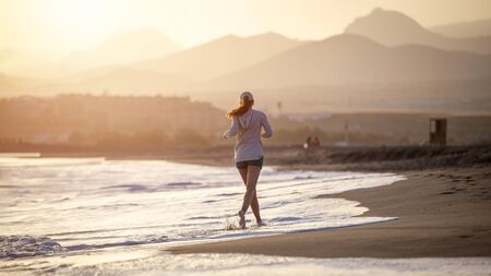 Young cheerful woman running on the ocean beach in the evening on summer vacationの写真素材