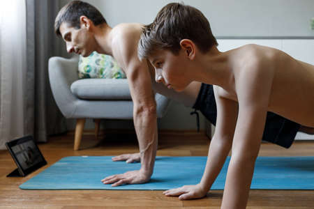 Young man with his son doing yoga at home on quarantine.